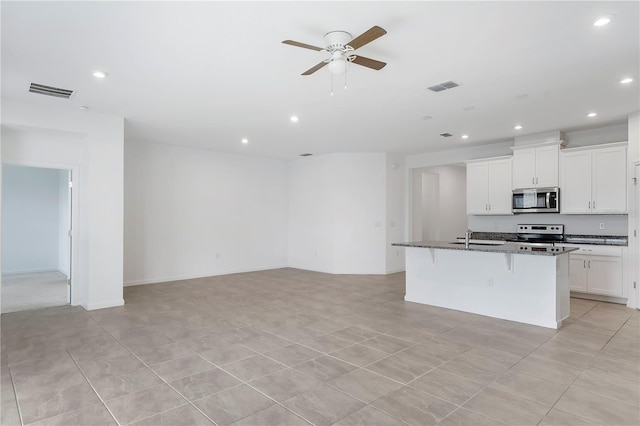 kitchen featuring a breakfast bar, sink, dark stone countertops, an island with sink, and stainless steel appliances