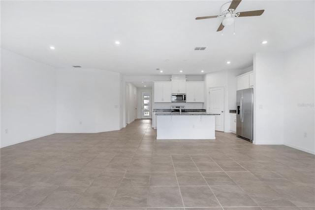 kitchen with appliances with stainless steel finishes, white cabinets, dark stone counters, a kitchen island with sink, and ceiling fan