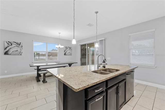 kitchen featuring sink, light stone counters, an island with sink, light tile patterned flooring, and decorative light fixtures