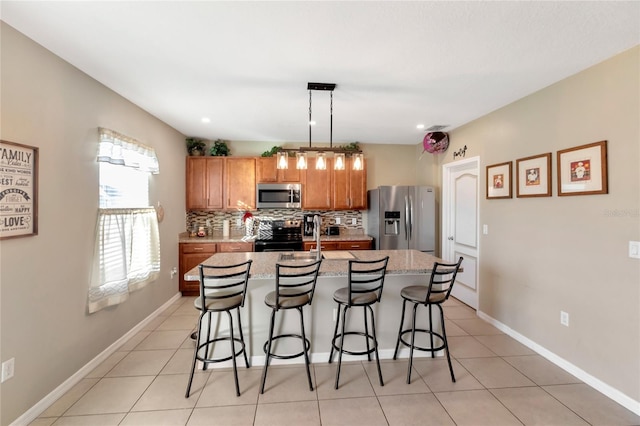 kitchen featuring a breakfast bar area, stainless steel appliances, decorative backsplash, a center island with sink, and decorative light fixtures