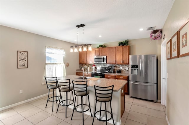 kitchen with pendant lighting, tasteful backsplash, an island with sink, sink, and stainless steel appliances