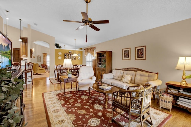 living room with ceiling fan, vaulted ceiling, a textured ceiling, and light wood-type flooring