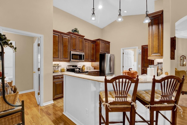 kitchen featuring decorative light fixtures, light hardwood / wood-style floors, a high ceiling, and appliances with stainless steel finishes