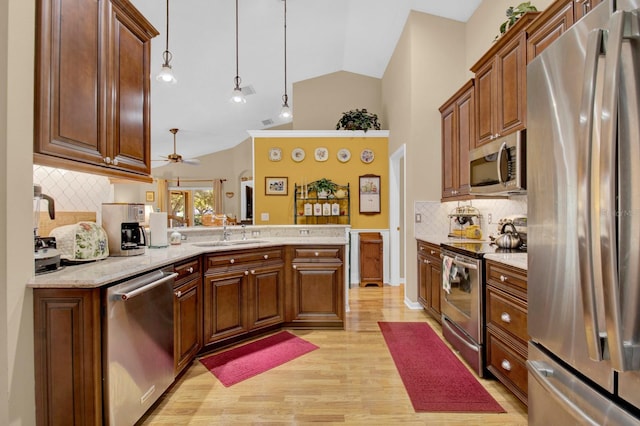 kitchen featuring appliances with stainless steel finishes, lofted ceiling, sink, hanging light fixtures, and light hardwood / wood-style flooring