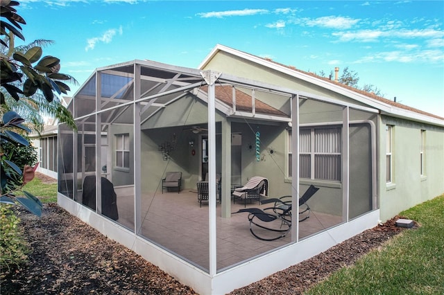 rear view of house with a patio, ceiling fan, and glass enclosure