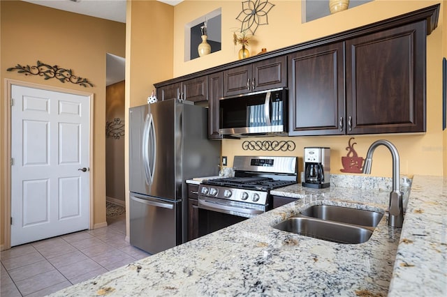 kitchen with dark brown cabinetry, sink, light stone counters, light tile patterned floors, and appliances with stainless steel finishes