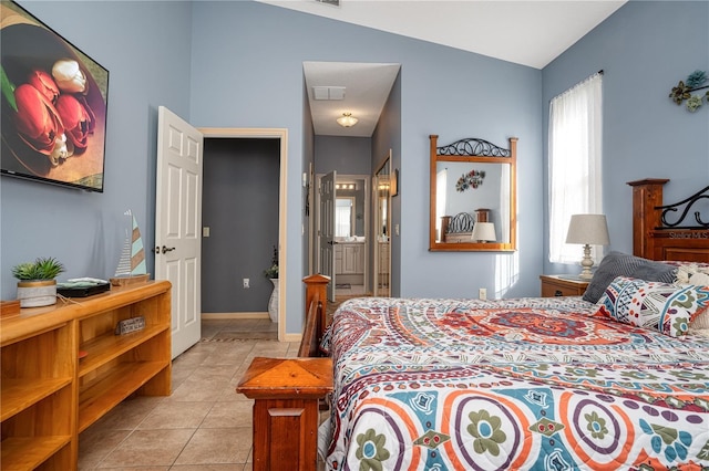 bedroom featuring lofted ceiling, light tile patterned floors, and ensuite bath