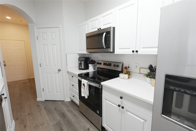 kitchen featuring white cabinetry, decorative backsplash, light wood-type flooring, and appliances with stainless steel finishes