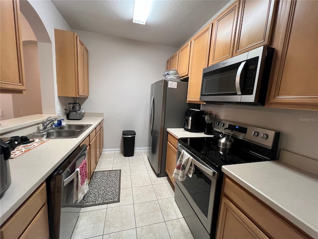 kitchen with appliances with stainless steel finishes, sink, light tile patterned floors, and a textured ceiling