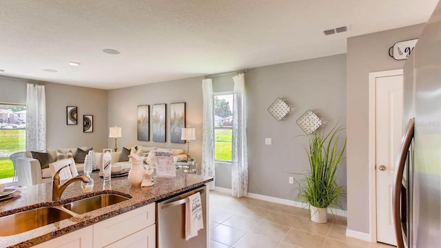 kitchen featuring sink, white cabinetry, light tile patterned floors, dark stone countertops, and dishwasher