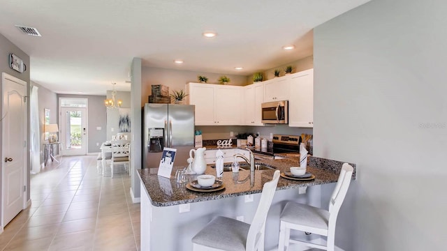 kitchen with light tile patterned flooring, appliances with stainless steel finishes, a breakfast bar area, dark stone counters, and kitchen peninsula