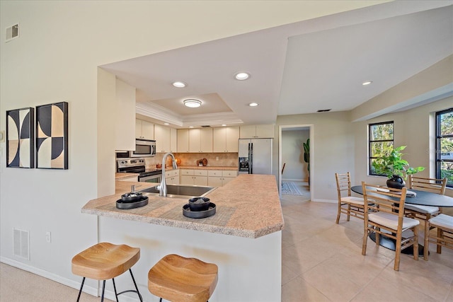 kitchen with appliances with stainless steel finishes, sink, a kitchen bar, kitchen peninsula, and a raised ceiling