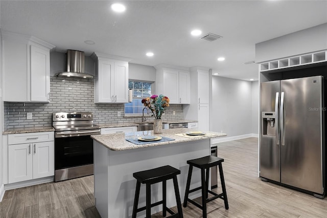 kitchen with wall chimney exhaust hood, a center island, stainless steel appliances, light hardwood / wood-style floors, and white cabinets