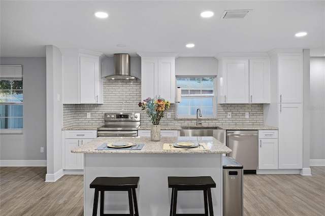 kitchen with sink, white cabinetry, a center island, stainless steel appliances, and wall chimney range hood