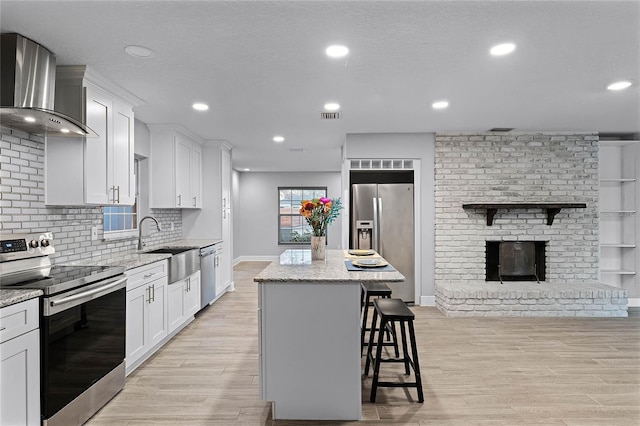 kitchen with stainless steel appliances, white cabinetry, a center island, and wall chimney exhaust hood