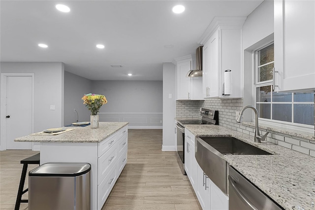 kitchen with appliances with stainless steel finishes, a center island, light stone counters, white cabinets, and wall chimney exhaust hood