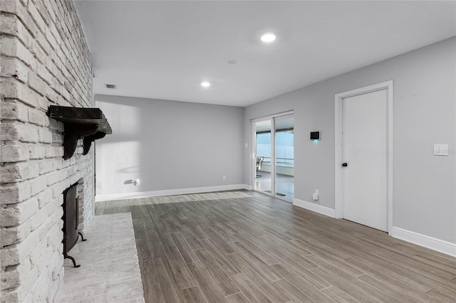 unfurnished living room featuring wood-type flooring and a brick fireplace