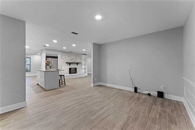 unfurnished living room with light hardwood / wood-style floors, a brick fireplace, and a textured ceiling