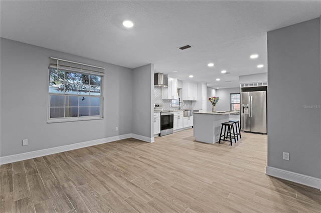 kitchen with a kitchen island, white cabinetry, a breakfast bar area, stainless steel appliances, and wall chimney exhaust hood