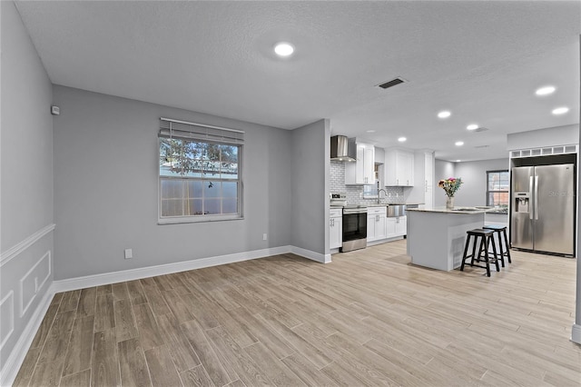 kitchen featuring wall chimney exhaust hood, a breakfast bar area, a center island, appliances with stainless steel finishes, and white cabinets