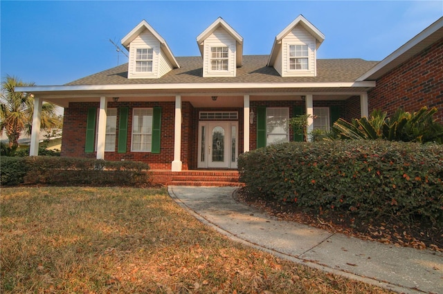 view of front of house with brick siding, a porch, a front yard, and roof with shingles