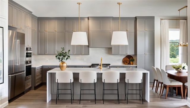 kitchen featuring gray cabinets, an island with sink, and built in refrigerator