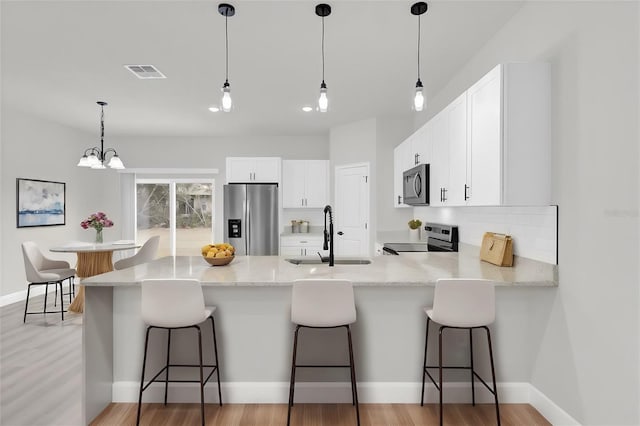 kitchen with sink, stainless steel appliances, light stone countertops, white cabinets, and kitchen peninsula