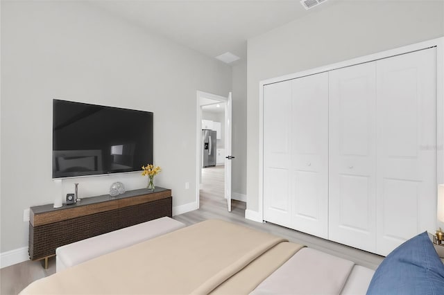 bedroom featuring stainless steel refrigerator with ice dispenser, hardwood / wood-style floors, and a closet