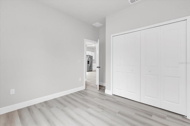 unfurnished bedroom with stainless steel refrigerator with ice dispenser, a closet, and light wood-type flooring