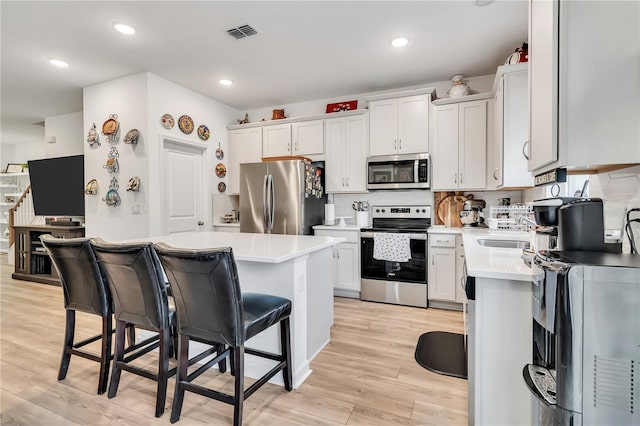 kitchen featuring a breakfast bar area, white cabinetry, appliances with stainless steel finishes, light hardwood / wood-style floors, and decorative backsplash