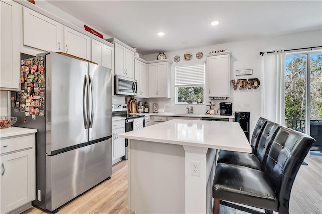 kitchen featuring white cabinetry, a kitchen breakfast bar, a center island, stainless steel appliances, and light hardwood / wood-style flooring