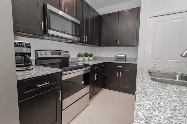 kitchen featuring appliances with stainless steel finishes, sink, light tile patterned floors, light stone countertops, and dark brown cabinets