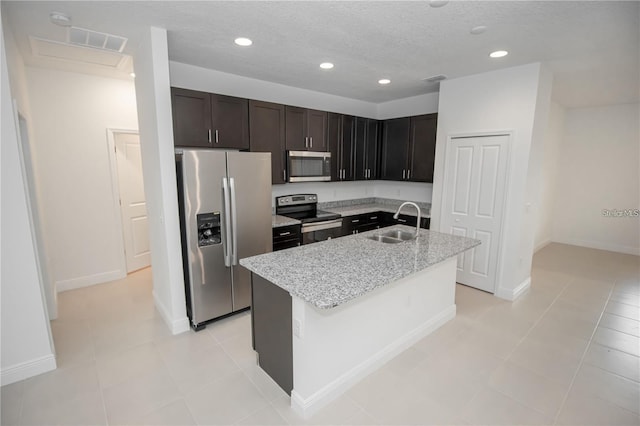 kitchen with sink, light stone counters, a textured ceiling, appliances with stainless steel finishes, and a kitchen island with sink