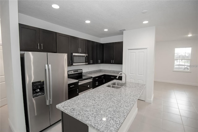 kitchen with sink, light tile patterned floors, appliances with stainless steel finishes, light stone countertops, and an island with sink