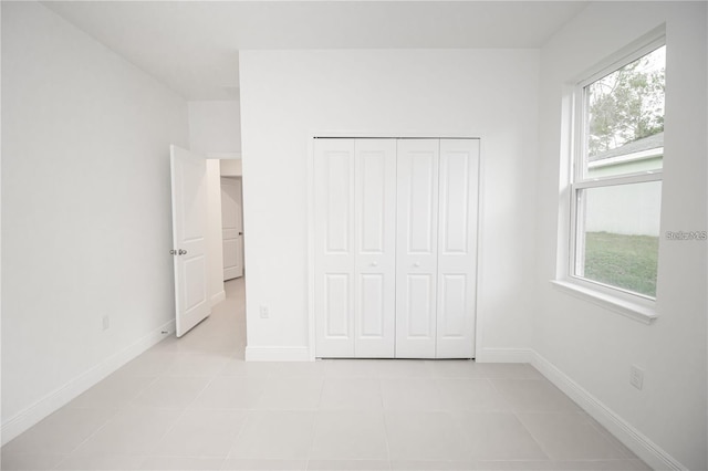 unfurnished bedroom featuring multiple windows, light tile patterned floors, and a closet