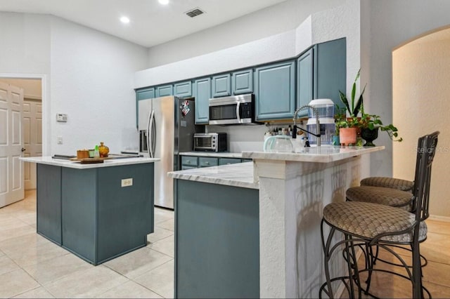 kitchen with blue cabinetry, a breakfast bar, light tile patterned floors, appliances with stainless steel finishes, and kitchen peninsula