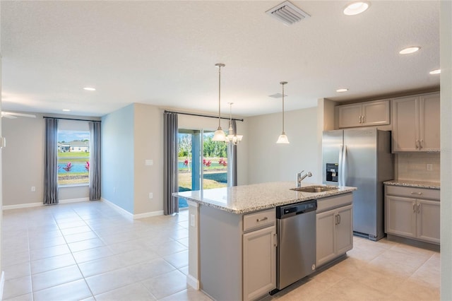 kitchen featuring sink, a center island with sink, appliances with stainless steel finishes, gray cabinets, and light stone countertops