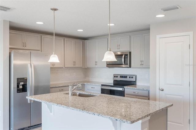 kitchen with pendant lighting, sink, a kitchen island with sink, stainless steel appliances, and light stone countertops