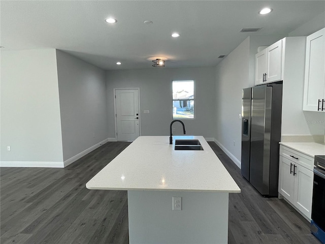 kitchen with sink, white cabinets, stainless steel fridge, light stone counters, and a center island with sink