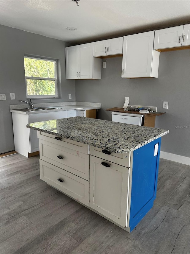 kitchen with sink, light stone counters, a kitchen island, hardwood / wood-style floors, and white cabinets