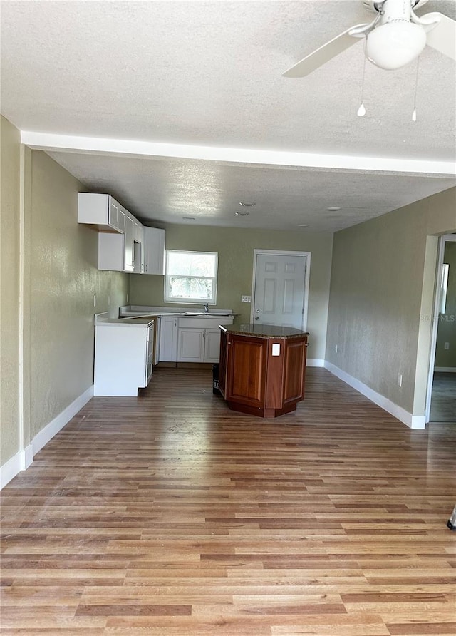 kitchen with a textured ceiling, a center island, white cabinets, and light wood-type flooring