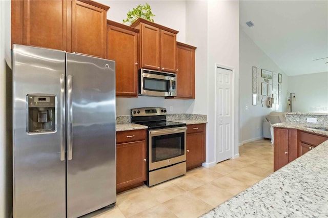 kitchen with light tile patterned flooring, sink, light stone counters, high vaulted ceiling, and stainless steel appliances