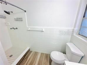 bathroom featuring a tile shower, tile walls, and toilet