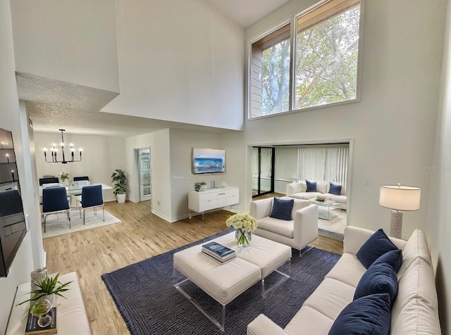 living room with a towering ceiling, a chandelier, a textured ceiling, and light hardwood / wood-style floors