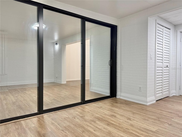 unfurnished bedroom with light hardwood / wood-style floors and brick wall