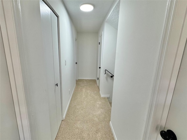 hallway with light carpet and a textured ceiling