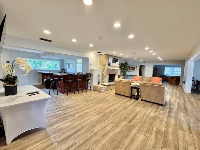 living room with bar, a stone fireplace, a wealth of natural light, and light hardwood / wood-style floors