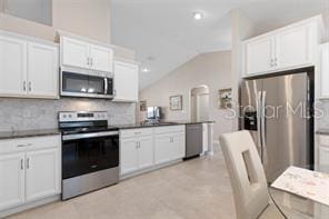 kitchen featuring white cabinetry, backsplash, stainless steel appliances, and lofted ceiling