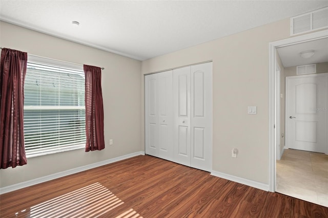 unfurnished bedroom with a closet, wood finished floors, visible vents, and baseboards