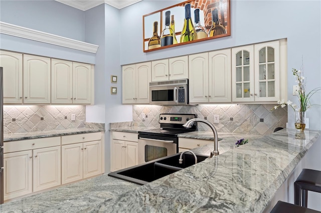 kitchen with backsplash, light stone countertops, kitchen peninsula, and appliances with stainless steel finishes